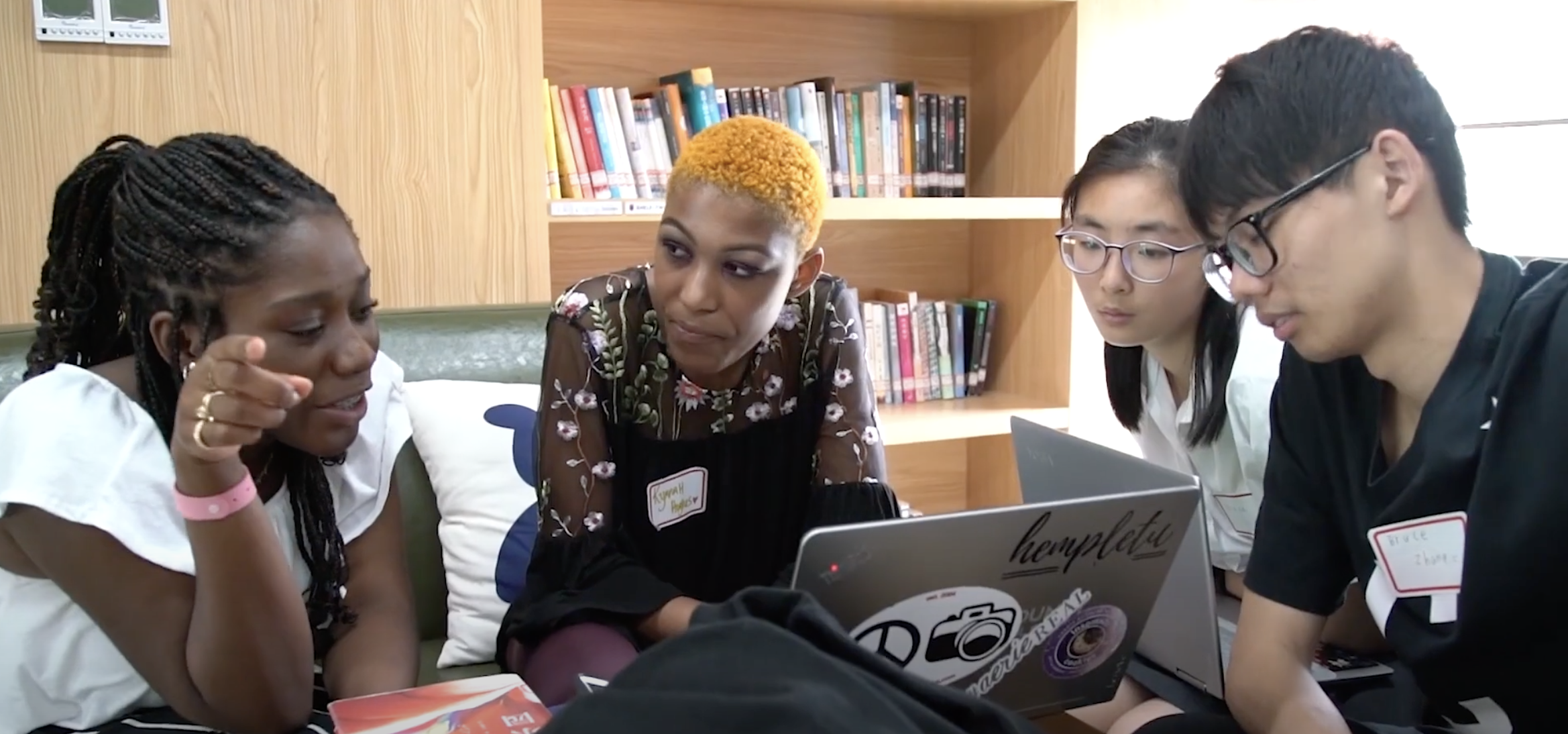 A group of students sit around a table of laptops in a library